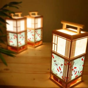 May include: Three rectangular wooden lanterns with light-colored frames and handles. Each lantern features a top section with white panels and a lower section decorated with a light blue pattern of red goldfish and swirling water motifs.