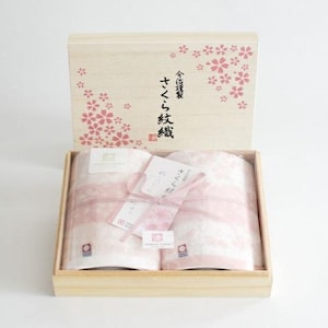 May include: Two pink towels with a white pattern are folded and tied with a pink ribbon in a wooden box. The box lid has a floral design and the text "さくら タオル 2枚組" in Japanese.