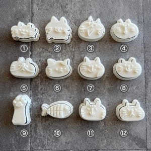 May include: Twelve white plastic cookie cutters shaped like cats and paws. The cutters are arranged in four rows of three. The cutters are numbered 1 through 12.