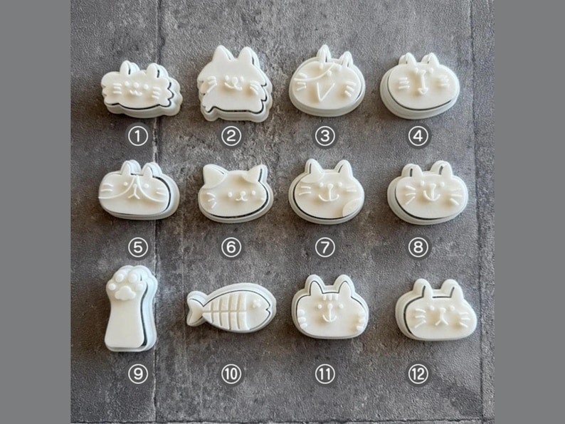 May include: Twelve white plastic cookie cutters shaped like cats and paws. The cutters are arranged in four rows of three. The cutters are numbered 1 through 12.