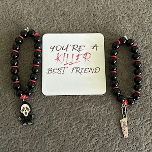 May include: Two black beaded bracelets with red accents and charms. One bracelet has a Ghostface charm, the other a knife charm that says "Killing it". A white card in the center reads "You're a Killer Best Friend".