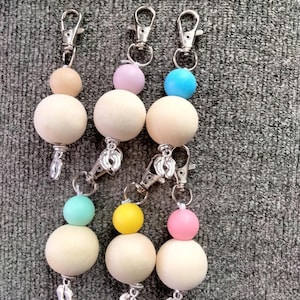 May include: Six wooden bead keychains with different colored beads and silver baby foot charms. The beads are pink, blue, yellow, and green.