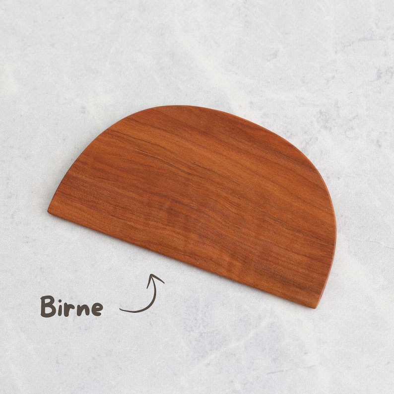 K&ouml;nnte beinhalten: Ein halbkreisf&ouml;rmiges Schneidebrett aus Holz in einem r&ouml;tlich-braunen Farbton. Das Brett hat eine glatte Oberfl&auml;che und ein nat&uuml;rliches Holzmaserungsmuster. Das Wort "Birne" ist auf der Oberfl&auml;che geschrieben.