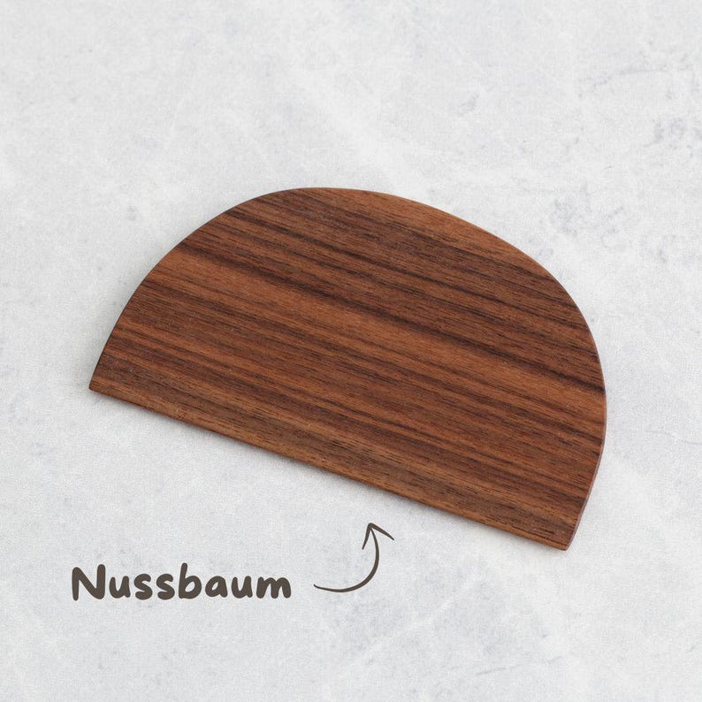 K&ouml;nnte beinhalten: Ein halbkreisf&ouml;rmiges Schneidebrett aus Holz mit einer dunkelbraunen Maserung. Unter dem Brett steht in handschriftlicher Schrift das Wort "Nussbaum", mit einem Pfeil.