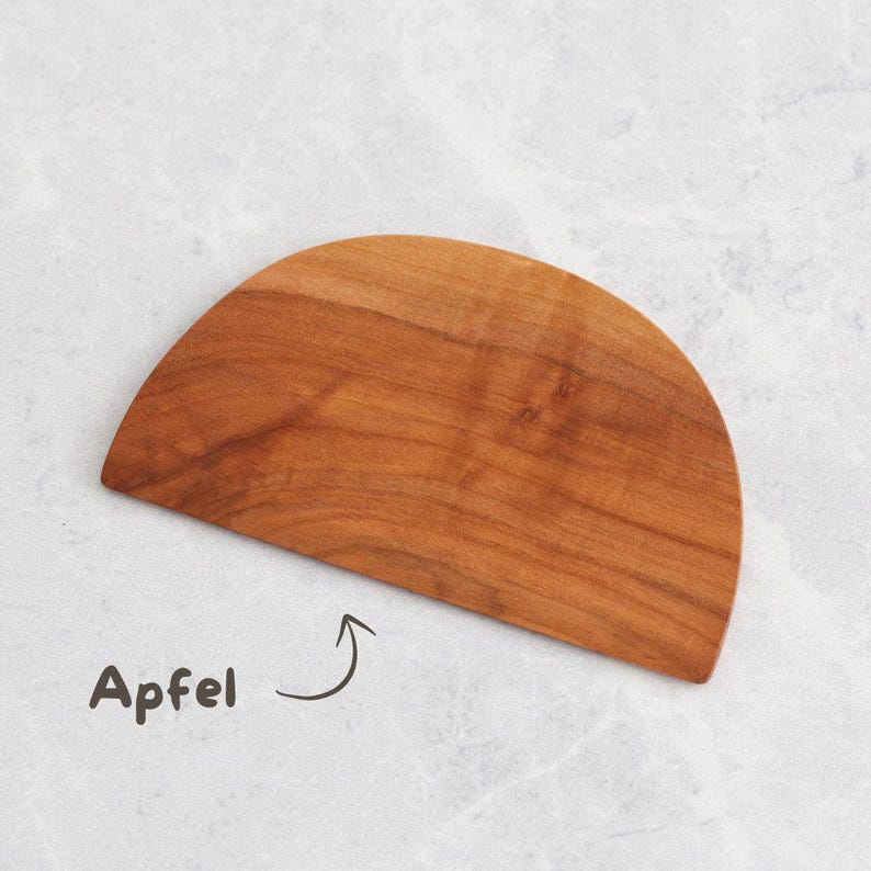 Ein halbkreisförmiger Teigschaber in einem warmen, rötlich-braunen Farbton. Die Holzmaserung ist sichtbar, und die Oberfläche ist glatt. Das Wort "Apfel" ist in Schwarz auf der linken unteren Seite des Bildes geschrieben.