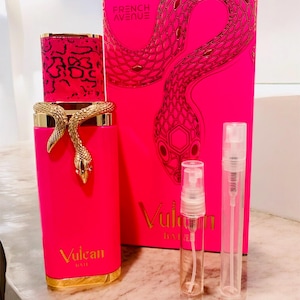 May include: A vibrant pink perfume bottle with a gold snake design and matching box. The bottle has a gold base and a patterned cap. The box features a snake illustration and the text "FRENCH AVENUE" and "Vulcan". Two small spray bottles are also present.