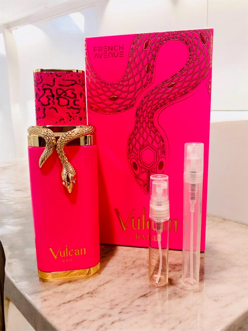 May include: A vibrant pink perfume bottle with a gold snake design and matching box. The bottle has a gold base and a patterned cap. The box features a snake illustration and the text "FRENCH AVENUE" and "Vulcan". Two small spray bottles are also present.