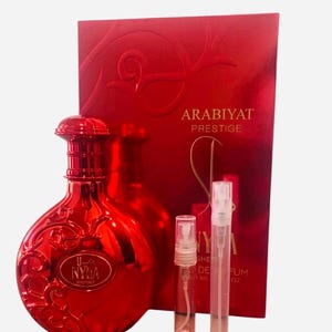 May include: A red perfume bottle with a matching box and two sample vials. The bottle has an ornate design and the brand name "NYLA" is visible. The box reads "ARABIYAT PRESTIGE".
