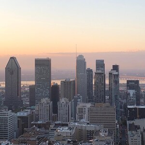 Puede incluir: Una vista panorámica de un horizonte urbano al amanecer. Los edificios son altos y modernos, con una mezcla de vidrio y hormigón. El cielo es de un rosa y naranja suave, con algunas nubes.
