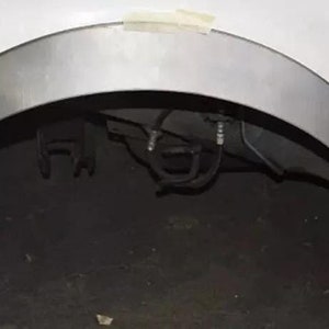 Pode incluir: Close-up de um arco de roda de um carro branco com uma extensão de pára-lamas de metal prateado. A extensão está presa com fita adesiva.