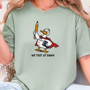 Camiseta divertida para profesores "We Test At Dawn" Camiseta Comfort Colors Regalo para el día de las pruebas estatales Camiseta de la semana de exámenes Sudadera Humor de agradecimiento al profesor Pato