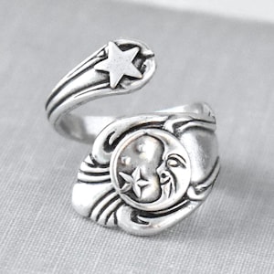 May include: Silver-toned adjustable ring featuring celestial designs. The ring showcases a crescent moon and star motif on the face, with a star accent on the band. The ring is made of a shiny, metallic material.