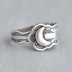 May include: A silver ring with a crescent moon design. The ring is made from a repurposed spoon and has an intricate design.