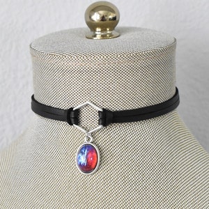May include: A black leather choker necklace with a silver hexagonal pendant and a red and blue oval-shaped glass charm.