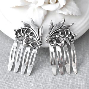 May include: A pair of silver-toned hair combs featuring a detailed relief design of lily of the valley flowers and leaves. Each comb has four sturdy prongs and an oxidised finish that highlights the intricate botanical textures on the decorative top.