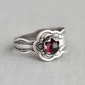 May include: A silver ring with an ornate design and a red gemstone in the center.