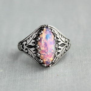 May include: A silver ring with an oval-shaped iridescent opal gemstone set in a filigree design.