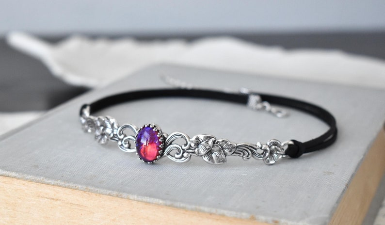 Puede incluir: Un collar gargantilla negro con un dise&ntilde;o floral plateado y una gran piedra preciosa ovalada iridiscente en el centro.