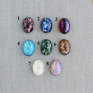Puede incluir: Ocho cabujones de vidrio ovalados con diferentes patrones y colores, incluyendo azul, verde, rojo y blanco. Los cabujones est&aacute;n numerados del 1 al 8.