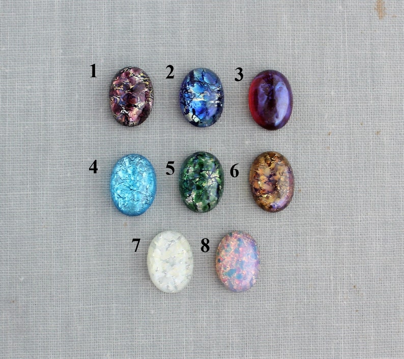 Puede incluir: Ocho cabujones de vidrio ovalados con diferentes patrones y colores, incluyendo azul, verde, rojo y blanco. Los cabujones est&aacute;n numerados del 1 al 8.