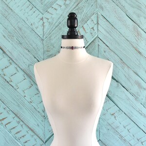 Puede incluir: Un collar gargantilla negro con una cadena plateada y un colgante de piedra roja.