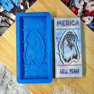 May include: A blue silicone mold and a finished soap bar with patriotic themes. The mold has the word "MERICA" and an eagle design. The soap bar features an eagle with a flag design and the words "MERICA" and "HELL YEAH!"
