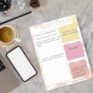May include: A "Heart Dump" notepad with handwritten notes and prompts. The notepad includes sections for "Pray," "Forgive," and "Do," with floral accents. A smartphone, coffee cup, and pencil are also visible.