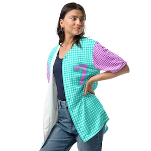 May include: A button-down baseball jersey with a turquoise and white gingham pattern. The sleeves are purple and white gingham. A large pink number 7 is on the front. The jersey is unbuttoned, revealing a navy blue shirt.