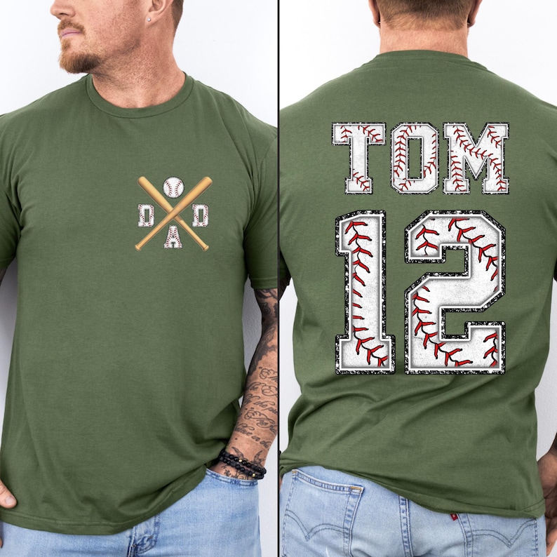 May include: Olive green baseball-themed t-shirt. The front features a crossed baseball bat and ball design with the word "DAD". The back displays the name "TOM" and the number "12", both with baseball stitching.