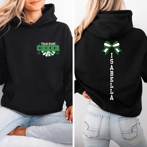 May include: Black hoodie with a green and white cheerleading design on the front and a white bow and the name "ISABELLA" on the back.