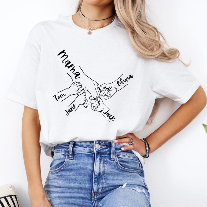 Puede incluir: Camiseta blanca con un dibujo de l&iacute;nea negra de manos que se agarran. El texto "Mama" est&aacute; en la parte superior del dise&ntilde;o, y los nombres "Tom", "Jane", "Olivia" y "Jack" est&aacute;n escritos a lo largo de los brazos.