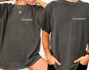 May include: Two charcoal gray t-shirts with the Roman numeral date XII.II.MMXIX printed in white. The shirts have a vintage, washed look and a relaxed fit. The image shows the shirts on two people.