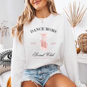 May include: White sweatshirt with the text "Dance Moms Est 2025 Social Club Weekends are for Dance" and a pair of pink ballet shoes.