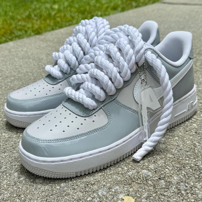 Puede incluir: Un par de zapatillas blancas y azul claro con gruesos cordones de cuerda blancos. Los zapatos tienen una suela blanca y un acento azul claro alrededor de la puntera y el tal&oacute;n. Una etiqueta transparente cuelga de los cordones.