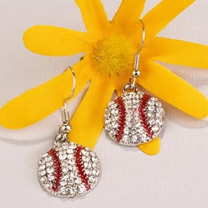 May include: A pair of silver earrings with red and white baseball charms. Each charm is covered in clear rhinestones.