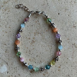 May include: A colorful bracelet with a silver chain and clasp. The bracelet features a variety of beads in pastel colors, including pink, blue, green, yellow, and orange. The beads are interspersed with small silver accents.