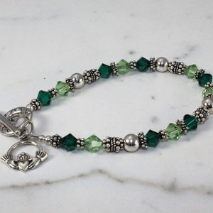 May include: A silver bracelet with green and light green crystal beads and a silver Claddagh charm.