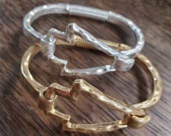 Pode incluir: Duas pulseiras de prata e ouro com um design de raio. As pulseiras estão empilhadas uma em cima da outra.