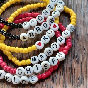 May include: A set of six colorful beaded bracelets with white letter beads spelling out the words "Chiefs", "Mahomes", "Arrow", "KC", "PA", and "Hea". Each bracelet has a small red heart bead.