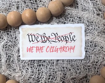 May include: A white sticker with the words "We the People" crossed out in red and the words "We the Oligarchy" written below in black.