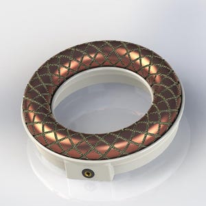 May include: A circular floral foam holder with a copper-colored, diamond-stitched top ring. The ring sits atop a white plastic base with a small, circular opening on the side. The design is modern and clean, suitable for floral arrangements.