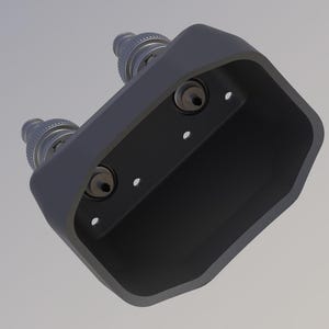 Könnte beinhalten: Ein schwarzer Kunststoffstecker mit drei silbernen Metallanschlüssen. Der Stecker hat eine rechteckige Form mit abgerundeten Kanten.