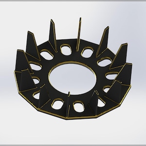 Puede incluir: Un anillo impreso en 3D negro y dorado con un centro circular y 12 bordes puntiagudos. El anillo tiene un diseño decorativo con una serie de pequeños agujeros alrededor del borde exterior.