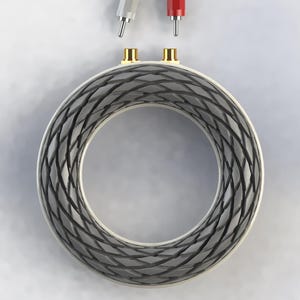 May include: A circular toroidal inductor featuring a dark grey, cross-hatched winding pattern around its core. Two gold-colored metal terminals are positioned at the top, with a white and a red connector plug hovering directly above them.