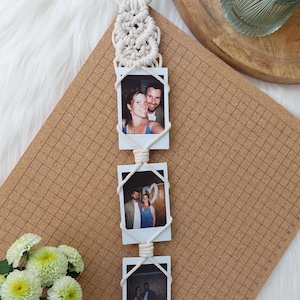 May include: A macrame photo display with three framed photos. The display features a wooden ring at the top, intricate knotting, and a tassel at the bottom. The photos are held in place with white rope.