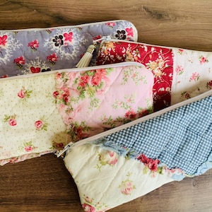 May include: Four quilted zipper pouches in various floral patterns. One pouch is lavender with pink and black flowers, another is red with yellow flowers, and a third is pink with red roses. The fourth pouch has a blue and white gingham pattern.