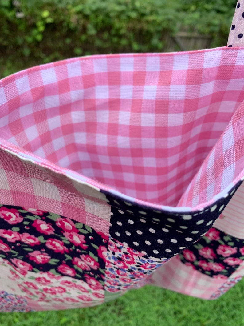 May include: A patchwork tote bag with a pink gingham interior. The exterior features a mix of floral, polka dot, and gingham patterns in shades of pink, navy, and white. The bag's handle is a pink polka dot fabric.