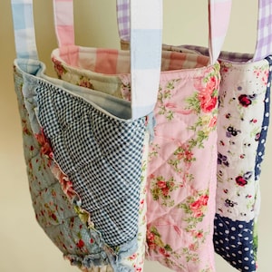May include: Three quilted tote bags with fabric straps. The bags feature floral, gingham, and polka dot patterns in shades of blue, pink, and white. The bags have ruffled edges and are designed for carrying items.