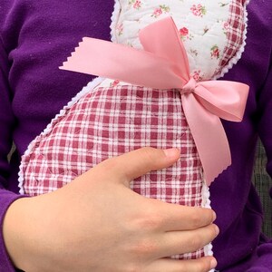 May include: A handmade cat-shaped pillow. The pillow features a white floral print fabric on the head and a red and white checkered pattern on the body. A pink satin bow adorns the neck, adding a decorative touch.