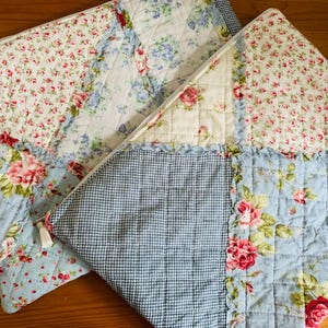 May include: Two quilted zippered pouches featuring a patchwork design of floral patterns with pink roses on white and light blue backgrounds, combined with a blue and white gingham check fabric. Each pouch has a white zipper closure with a small tassel.
